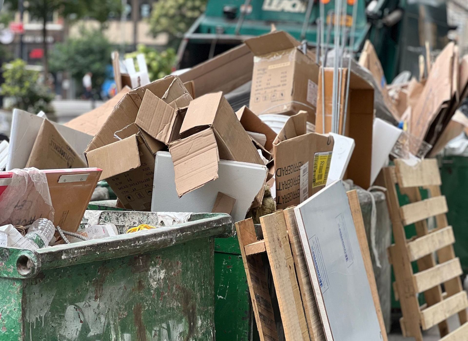 Piled cardboard boxes and waste in a city dumpster highlight urban recycling.