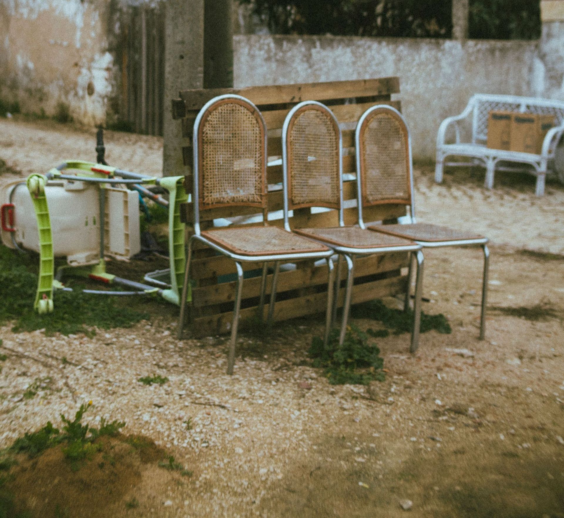 Weathered wooden chairs and vintage furniture in a rustic outdoor setting.